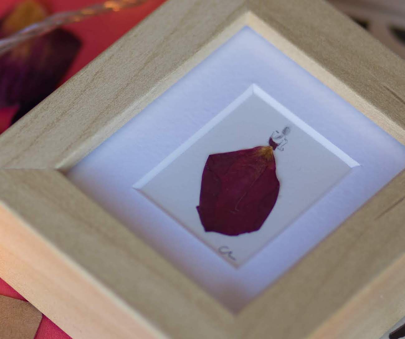 This artwork is a representation of a figure in a red ball gown, meticulously crafted from a single rose petal to capture the flowing lines and bold colour of the dress.